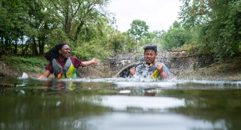 two teens splash each other in water on a canoeing trip with outward bound